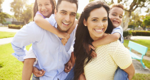 Parents Giving Children Piggyback Ride In Garden